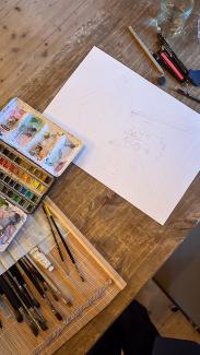 an image captured during the process of a live drawing of a wedding. The wedding couple sketched with pencil, tools around the paper, a personal artwork in progress